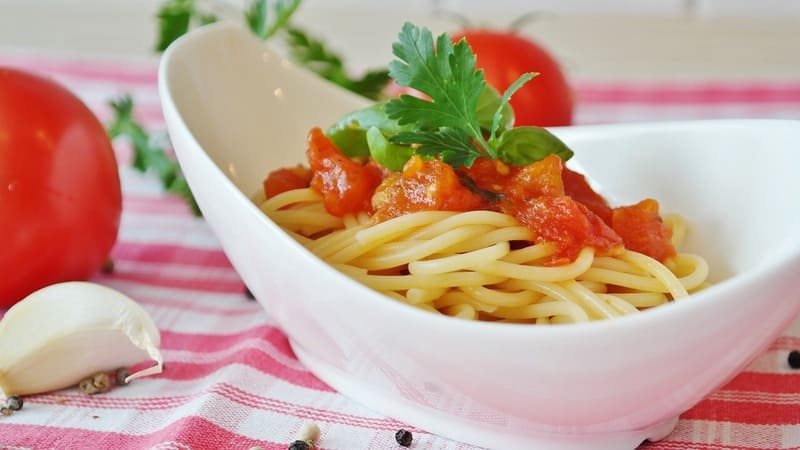 ランチョンマットの上にある白いお皿に盛りつけられたトマトスパゲッティ