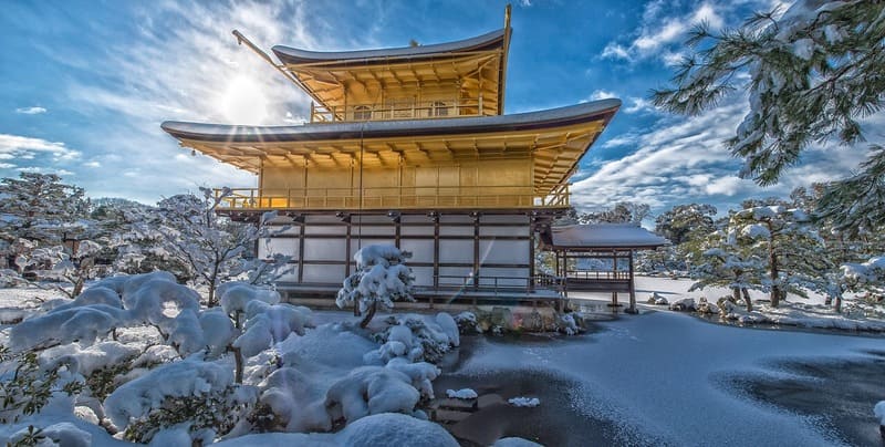 太陽と青空の中の雪の積もった金閣寺